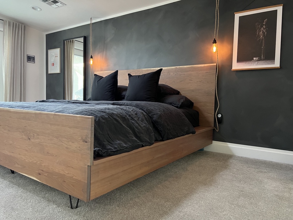 Live-edge white oak platform bed with black hairpin legs and dark linen bedding